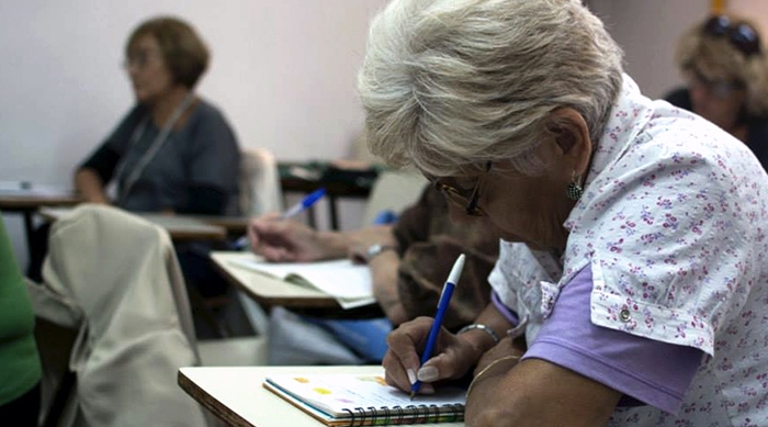 Una mujer adulta mayor escribiendo en un aula.